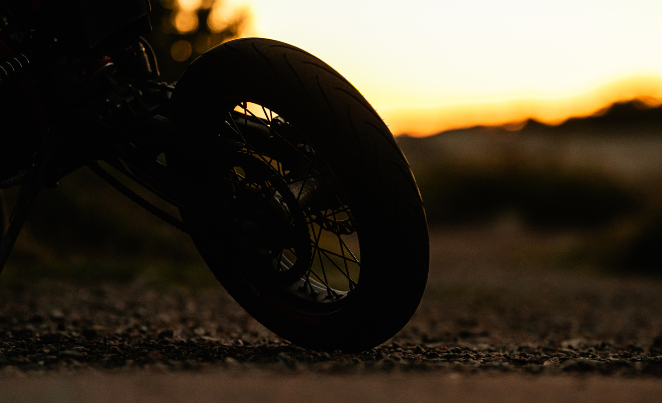 Motorcycle silhouette on gravel road at dusk.